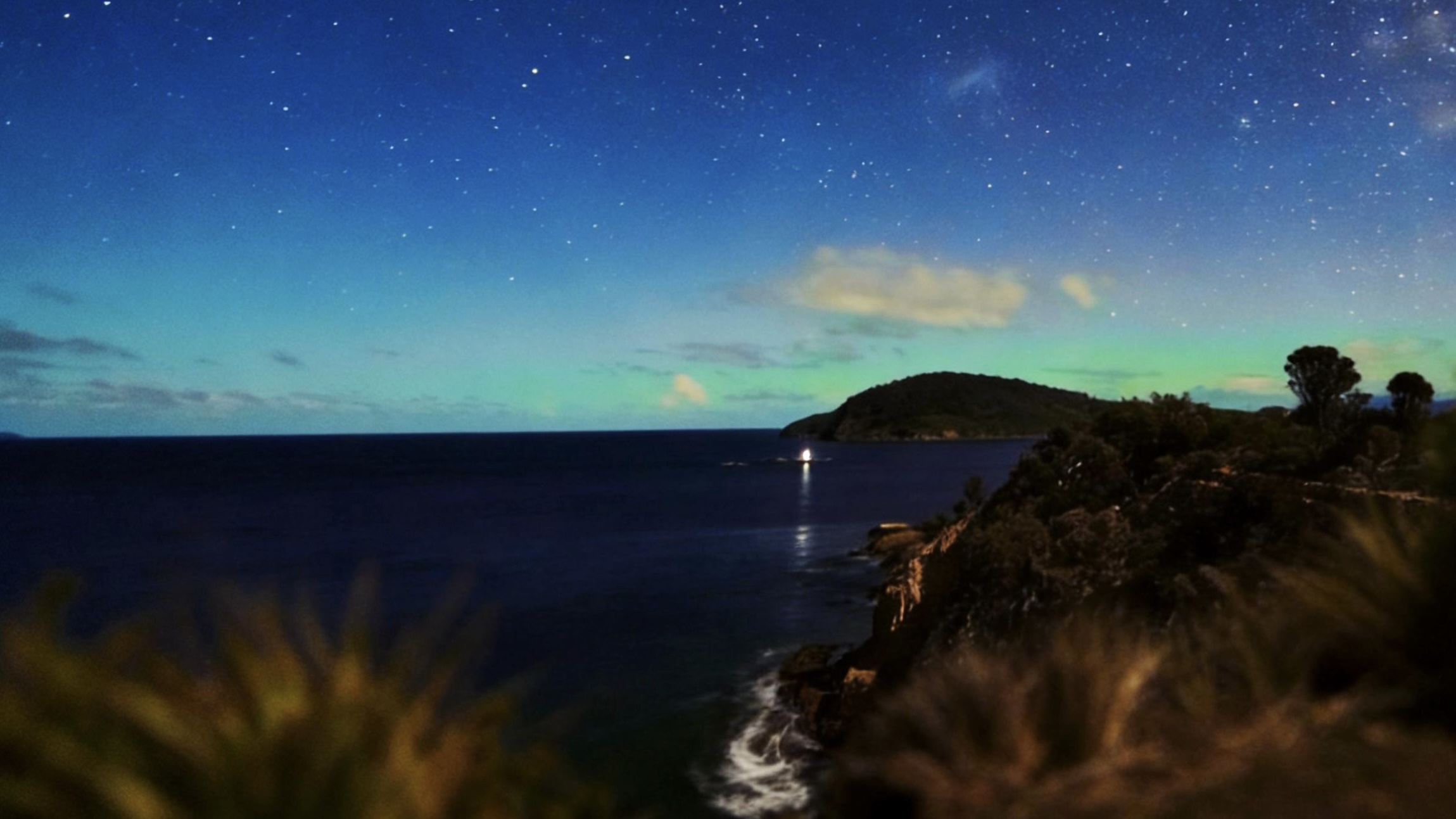 星空下的海岸与远处山丘，深蓝海面上有一点灯光